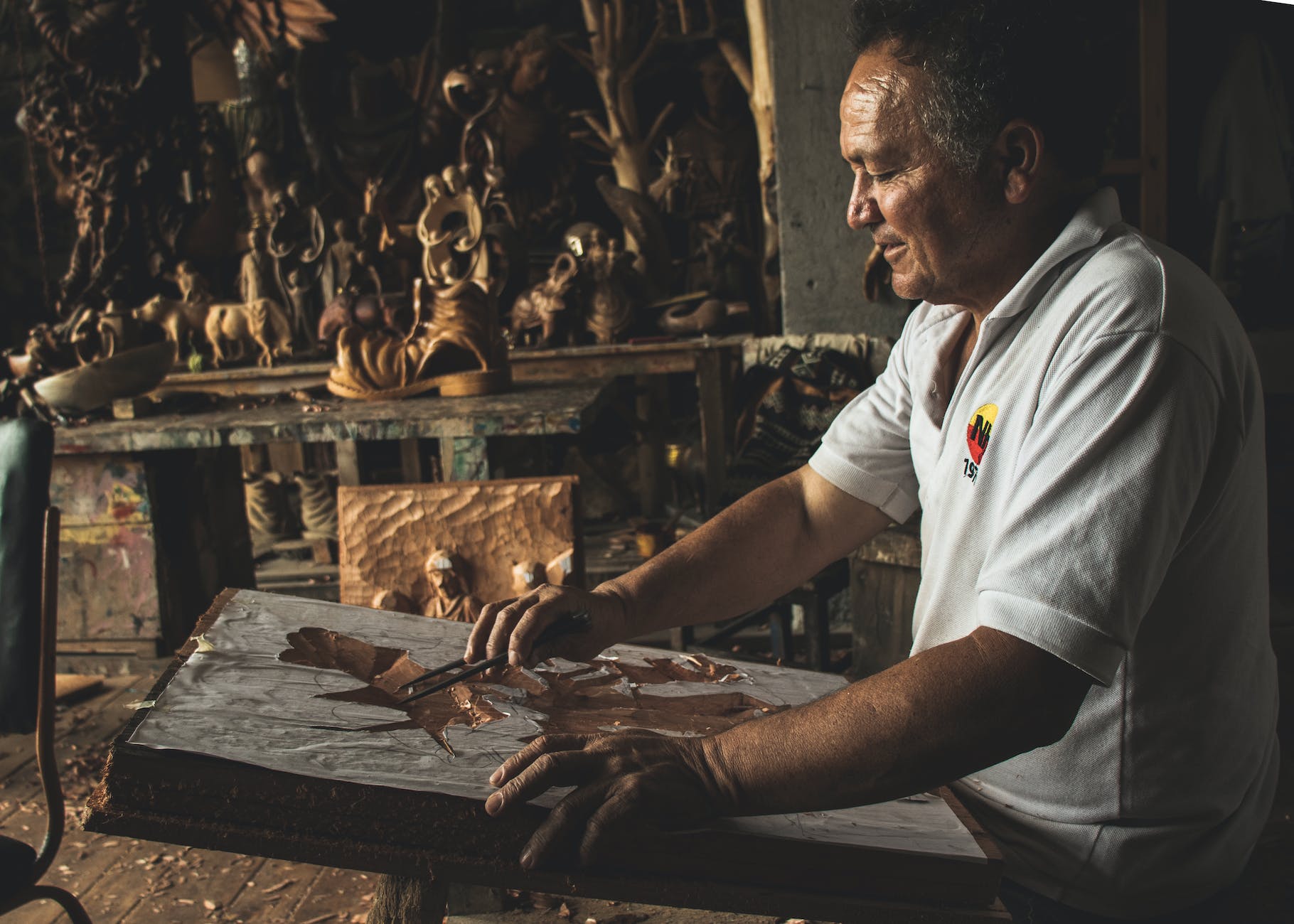 man in white polo shirt working on wooden sculpture