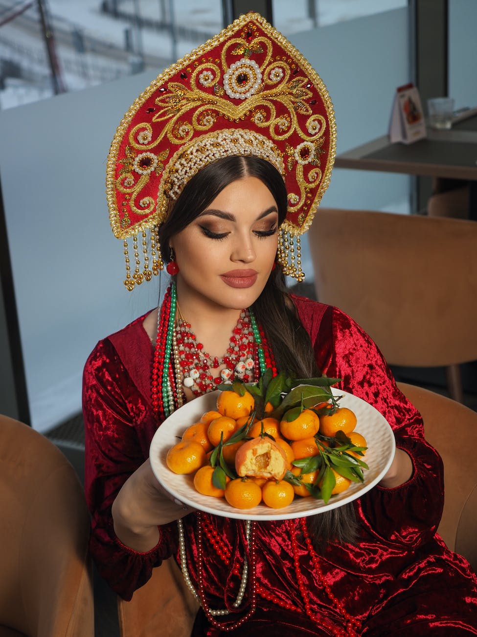 woman wearing ornamental hat and red velvet dress holding plate with tangerines