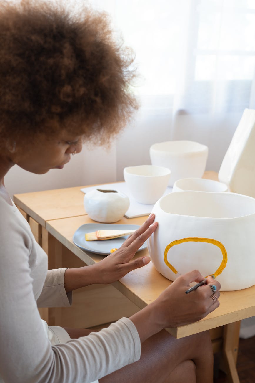 skilled black craftswoman painting on ceramic earthenware in studio