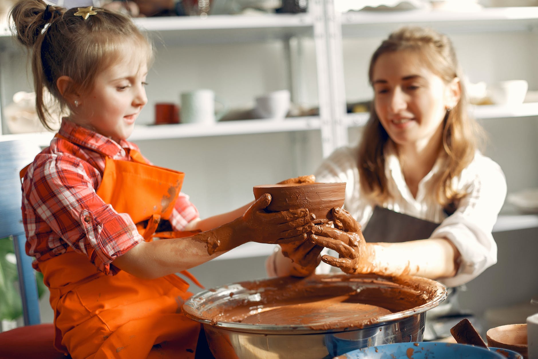 happy little girl making ceramic bowl with mother in pottery
