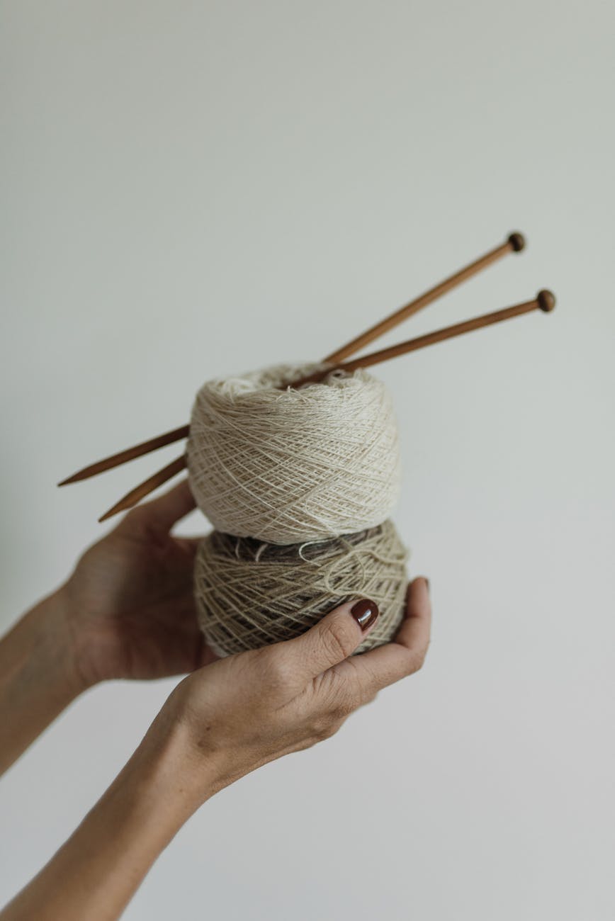a person holding a thread with knitting pins
