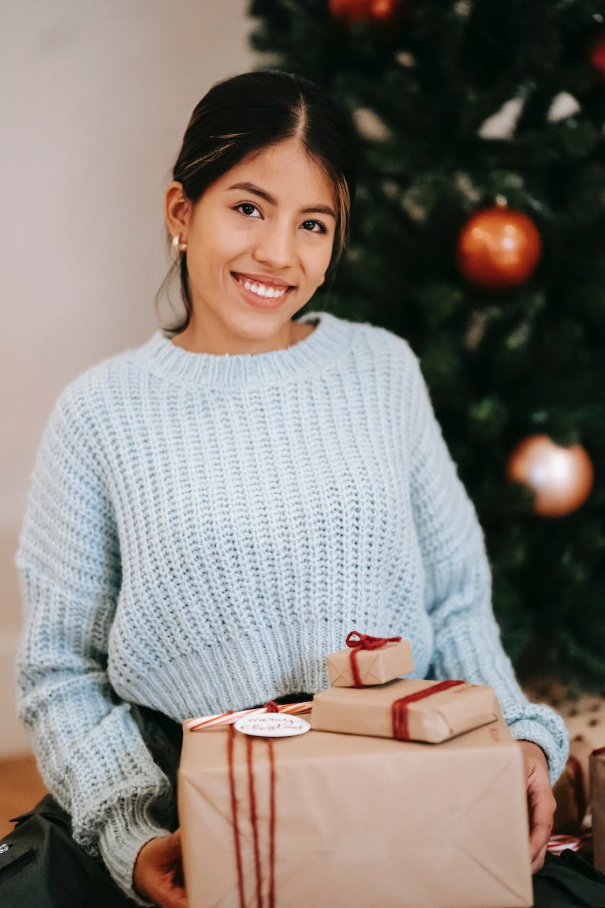 sincere ethnic woman with pile of gift boxes at home
