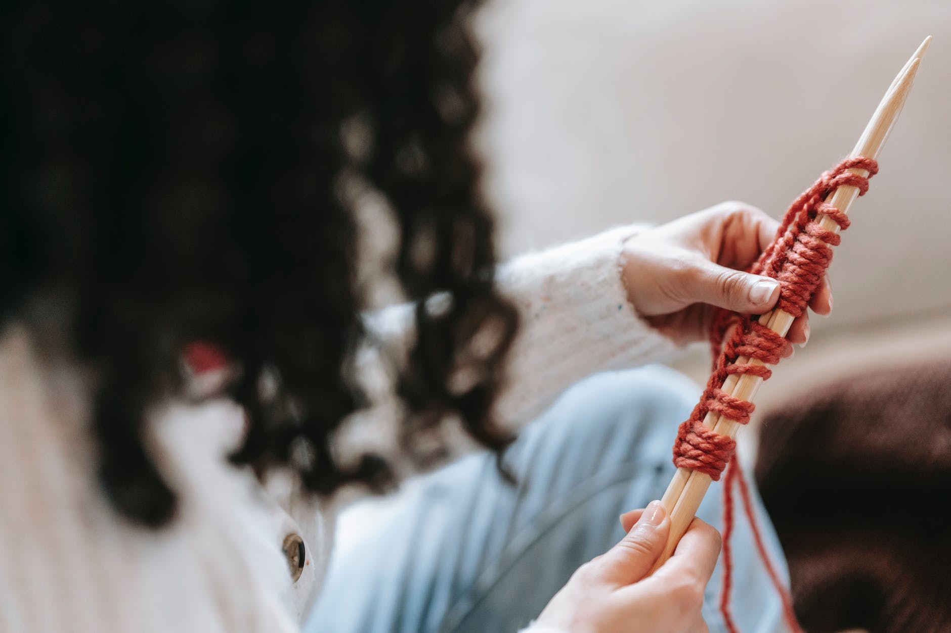 crop unrecognizable woman tying thread on needles while knitting at home