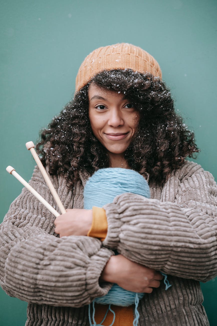 smiling black artisan with yarn and knitting needles in winter