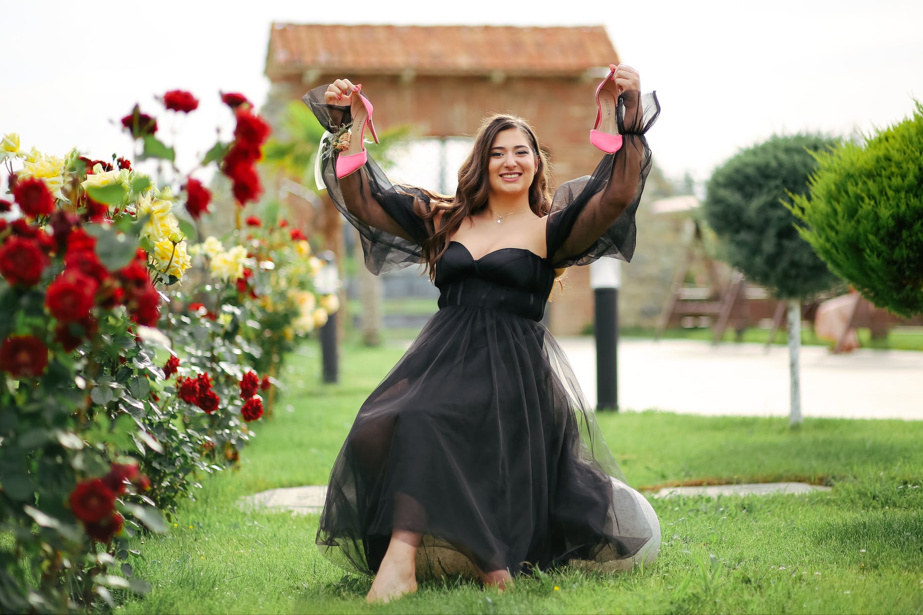 young woman in a black dress sitting in the garden and holding her shoes up