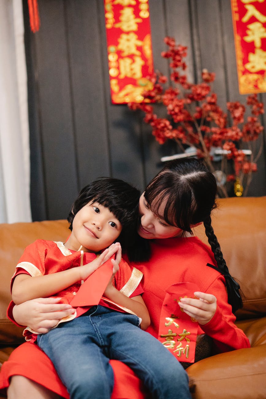 asian teen embracing brother with red envelope on sofa